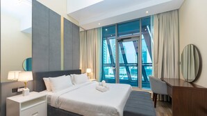 A modern hotel room with a large bed, a desk, and a view of a cityscape through large windows. - Stunning Corner Suite Canal View (Dubai)