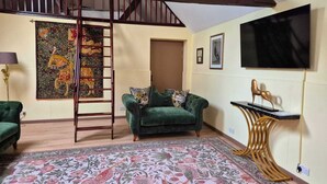 Een kamer met een groene bank, een ladder, een kamerbreed tapijt met dessin, een wandtelevisie en een decoratief paardenbeeld.