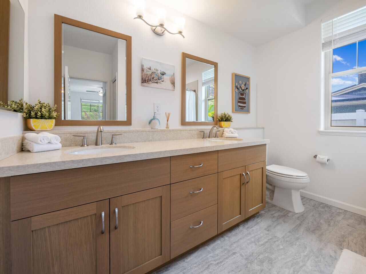 A bathroom with a wooden vanity, a sink, a toilet, and a window with blinds.