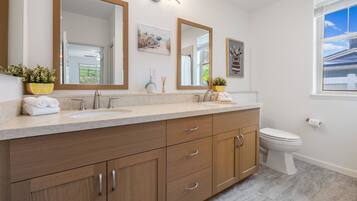 A bathroom with a wooden vanity, a sink, a toilet, and a window with blinds.