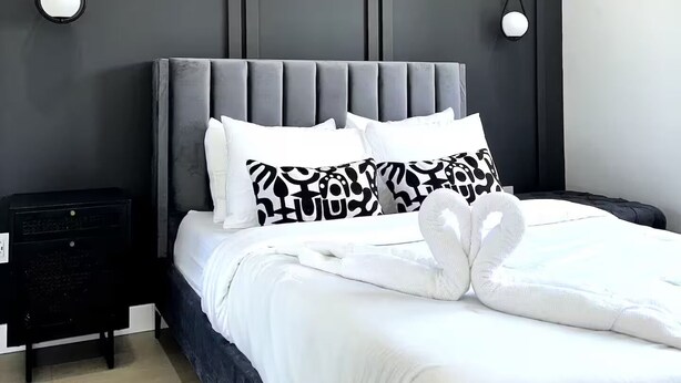 Une chambre moderne avec une tête de lit rembourrée de couleur grise, une literie blanche et deux appliques murales.