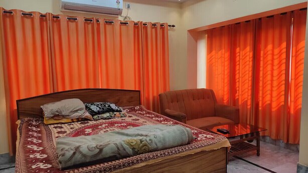 Une chambre à coucher avec un lit en bois, des rideaux orange, une chaise et une petite table.