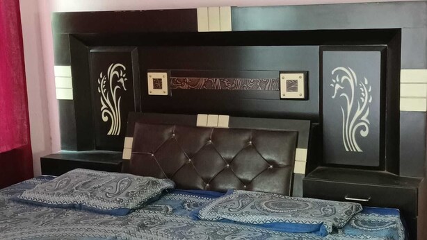 Un dormitorio con cabecera oscura, paneles decorativos en la pared y colcha estampada.