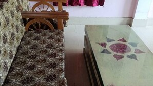 Una habitación con un sofá estampado, una silla de madera y una mesa de centro con cubierta de vidrio y diseño geométrico.
