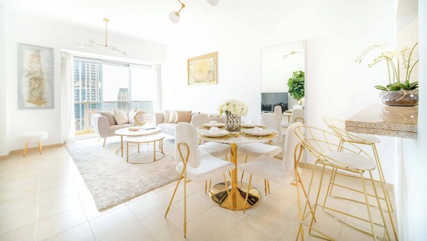A modern living room with a round gold table, white sofas, and a large window. - Marina Tower 2602 (Dubai)