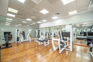 A gym with various exercise machines, a wooden floor, and a large mirror wall. - Marina Tower 2602 (Dubai)