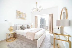 A modern bedroom with a large bed, a glass table, a mirror, and a view of tall buildings. - Marina Tower 2602 (Dubai)