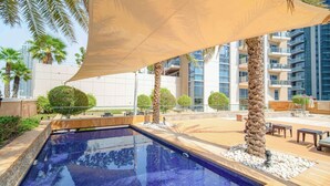 A swimming pool with a tiled deck, surrounded by palm trees and a large canopy.
