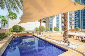 A swimming pool with a tiled deck, surrounded by palm trees and a large canopy.