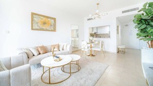 A modern living room with a sofa, two round tables, a dining area, and a kitchen in the background. - Marina Tower 2602 (Dubai)