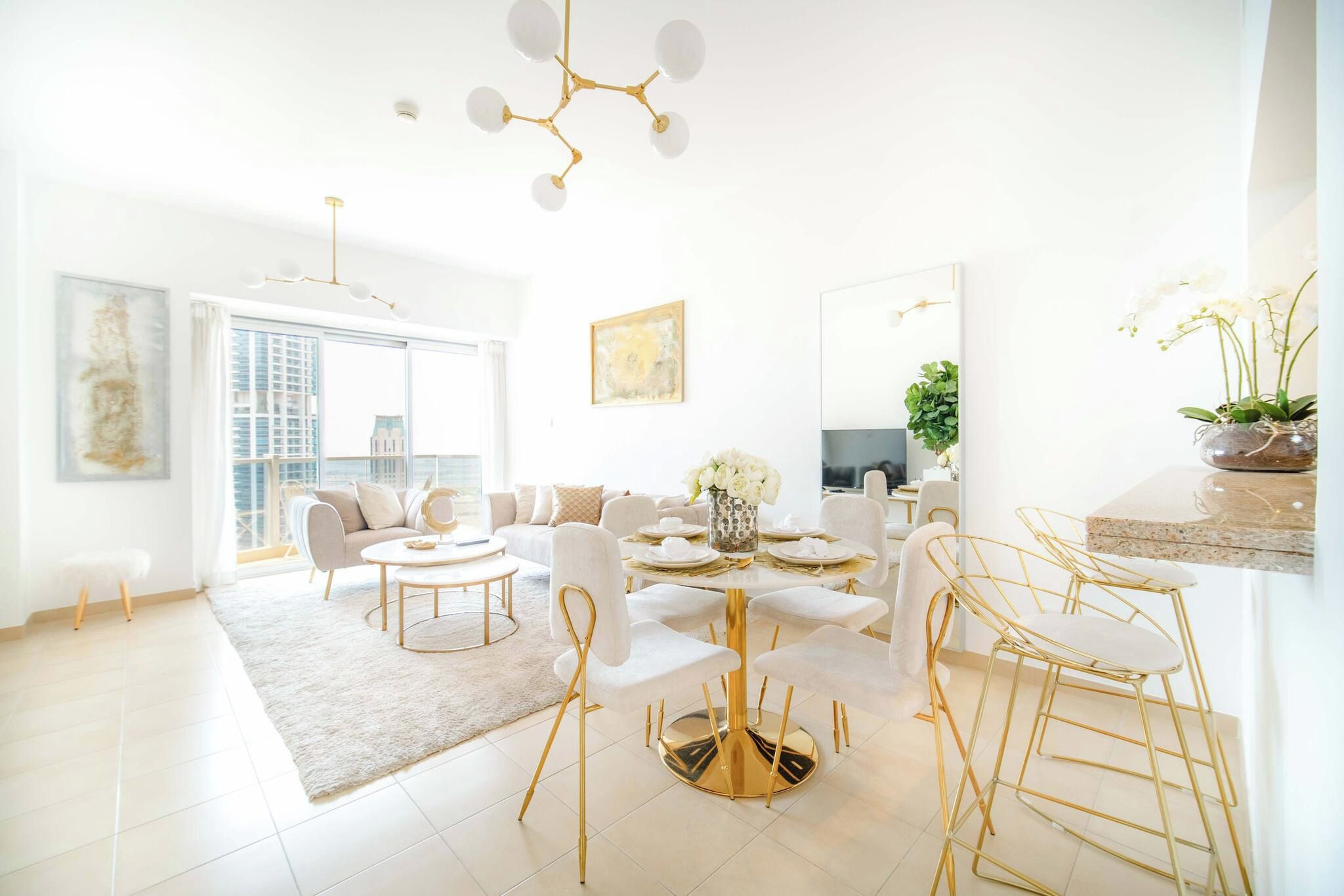Un salon moderne avec une table ronde dorée, des canapés blancs et une grande fenêtre.