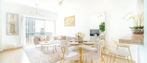 Un salon moderne avec une table ronde dorée, des canapés blancs et une grande fenêtre.