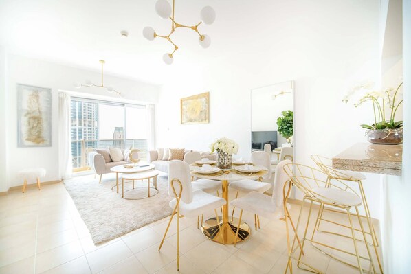A modern living room with a round gold table, white sofas, and a large window.