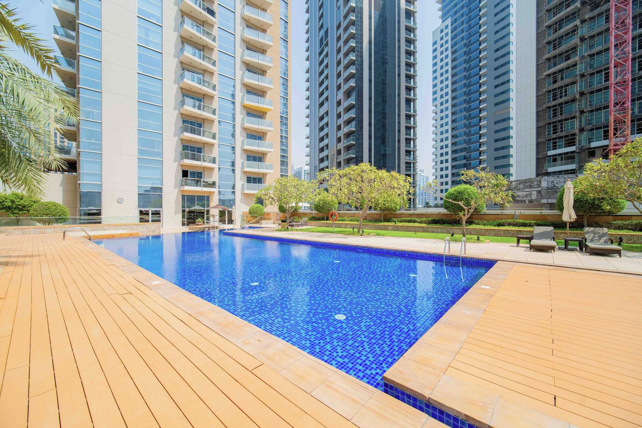 Una piscina rodeada de una cubierta de madera, con edificios residenciales altos al fondo.