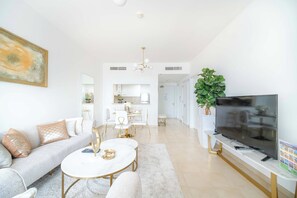 A modern living room with a sofa, coffee table, and TV. There is a dining area with a white table and chairs. - Marina Tower 2602 (Dubai)