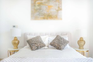 A neatly arranged bedroom with a bed, two nightstands, and a wall-mounted abstract painting.