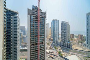 A high-rise building with a construction crane, surrounded by other tall buildings and a busy street.