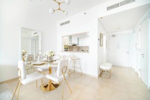A modern dining area with white furniture and gold accents, a kitchen in the background, and a clean, bright interior. - Marina Tower 2602 (Dubai)