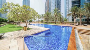 A swimming pool with tiled blue floor, surrounded by palm trees and a grassy area. - Marina Tower 2602 (Dubai)