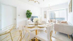 A modern dining area with a white table set for four, gold chairs, and a chandelier. - Marina Tower 2602 (Dubai)