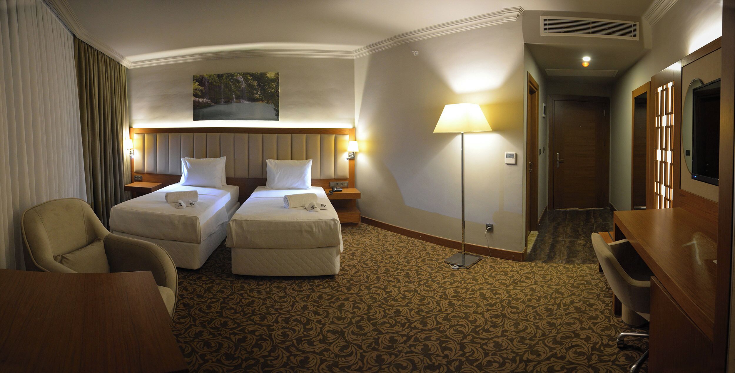 Une chambre d’hôtel avec deux lits, un bureau, une chaise, une lampe et un tableau au mur.