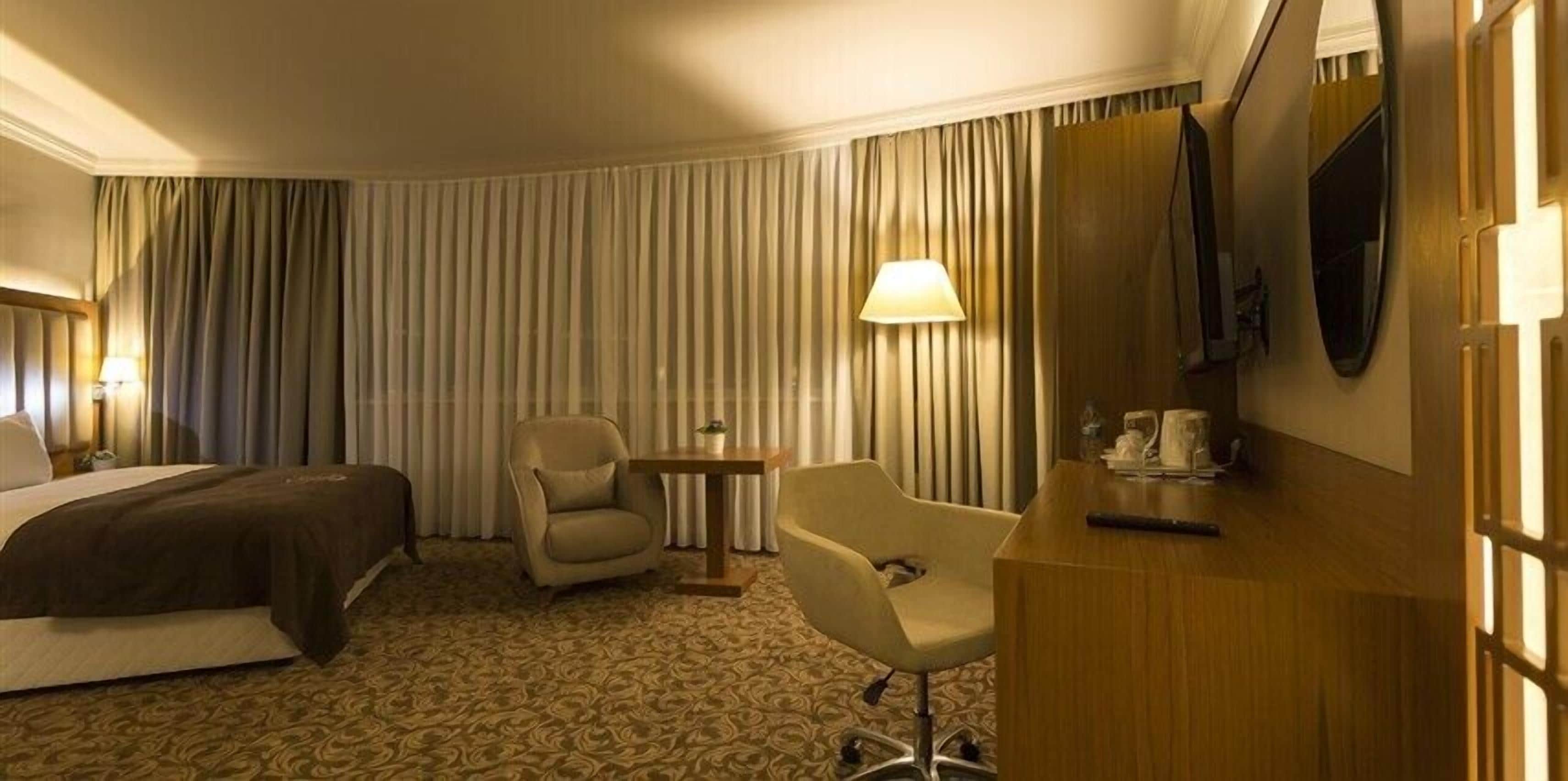 Ein Hotelzimmer mit Bett, Sessel, kleinem Tisch mit Lampe und an der Wand befestigtem Fernseher.