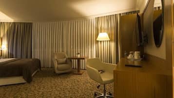 Ein Hotelzimmer mit Bett, Sessel, kleinem Tisch mit Lampe und an der Wand befestigtem Fernseher.