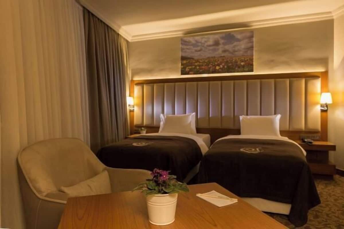 Habitación de hotel con dos camas, una mesa de madera, una silla y un cuadro en la pared.