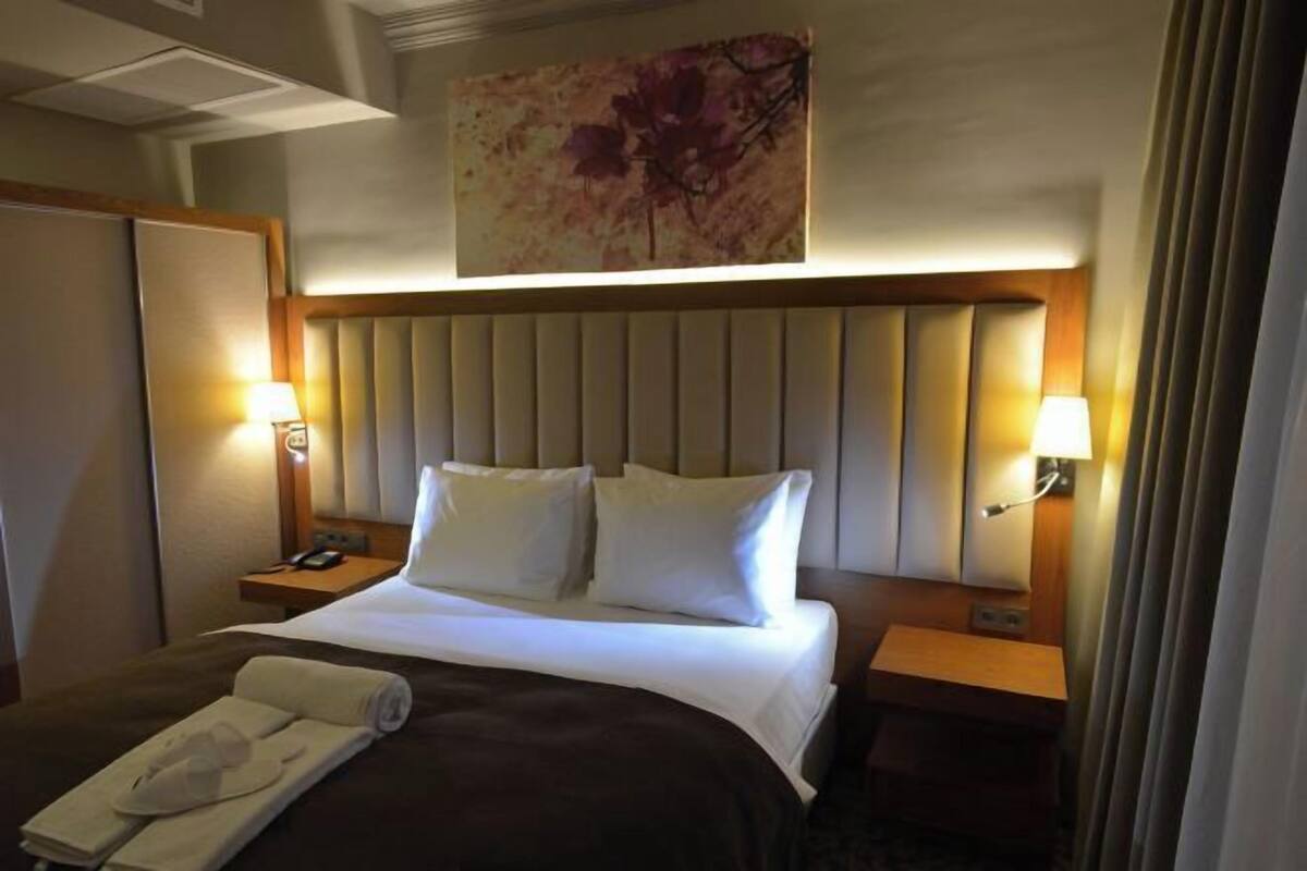 Una habitación de hotel con una cama grande, dos mesitas de noche y un cuadro colgado en la pared.
