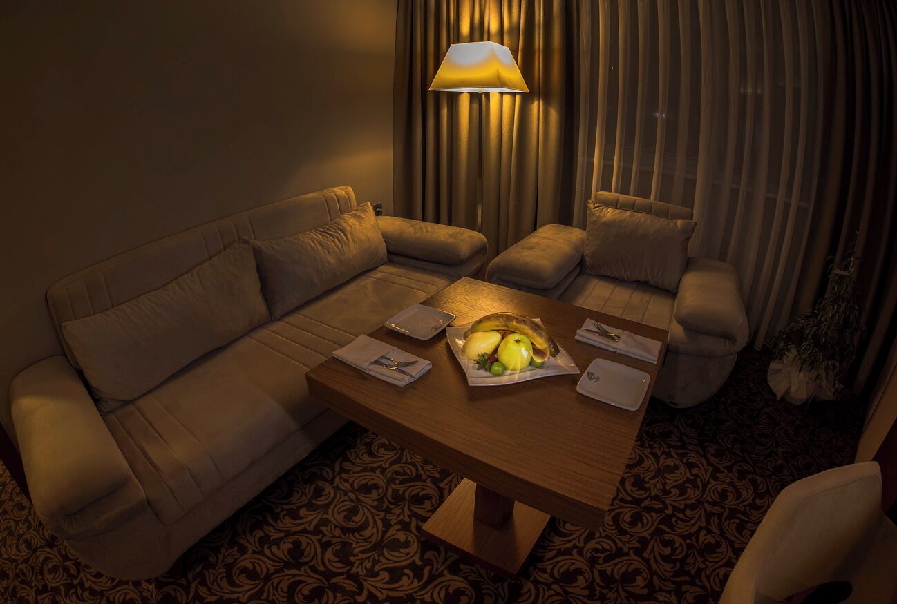 Et hyggeligt hotelværelse med sofa, lænestole, et træbord med en frugtkurv og en lampe.