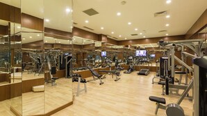 A modern gym with mirrored walls, various exercise equipment, and a wooden floor.