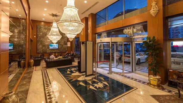 A hotel lobby with a marble floor, a reception desk, a seating area, and a glass elevator.