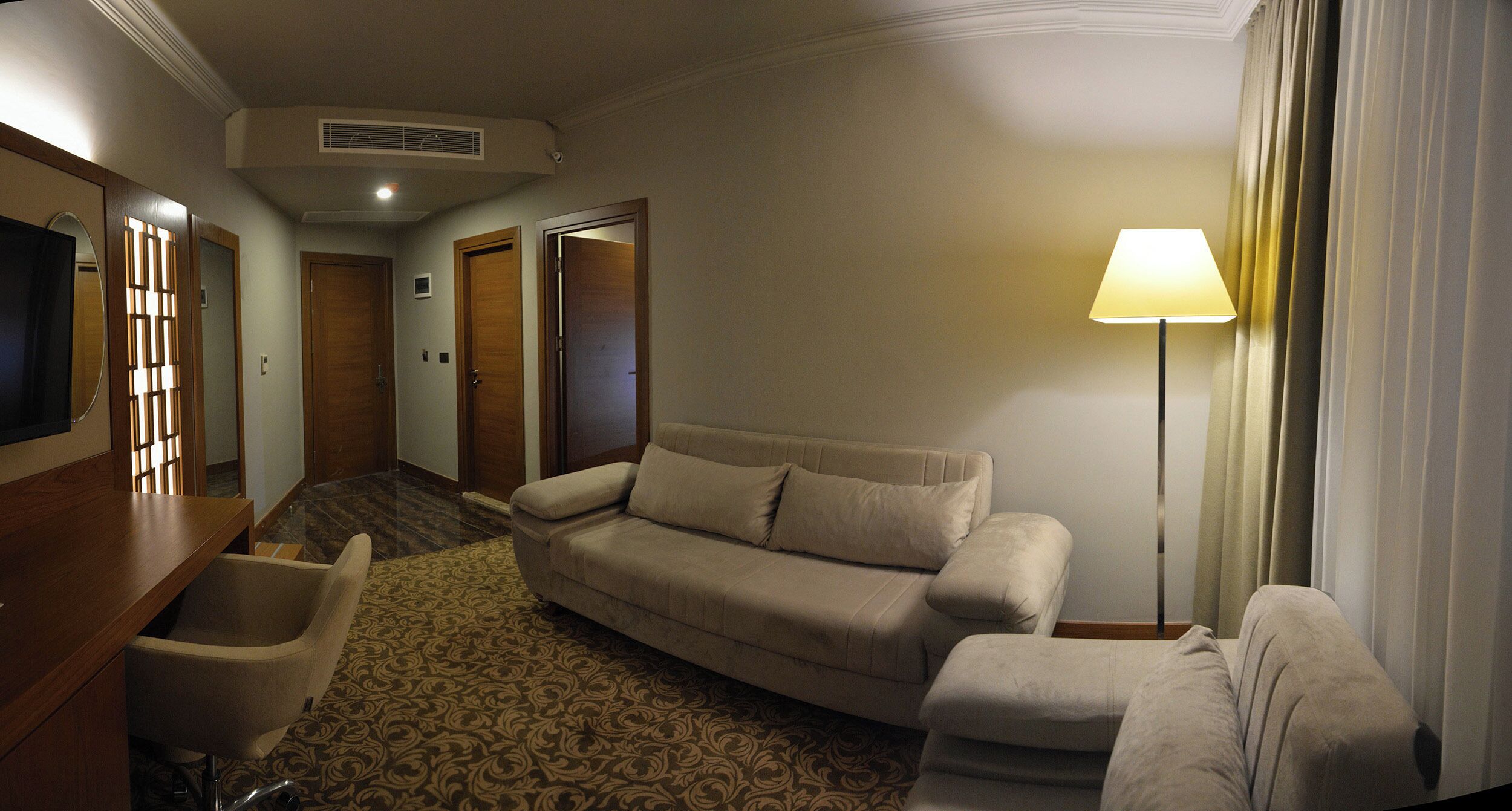 Une chambre d’hôtel avec un canapé, un fauteuil, une lampe et un téléviseur.