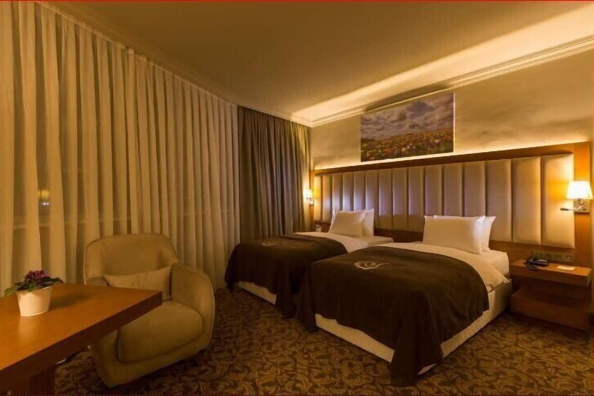 Habitación de hotel con dos camas, un escritorio, una silla y un ventanal con cortinas.