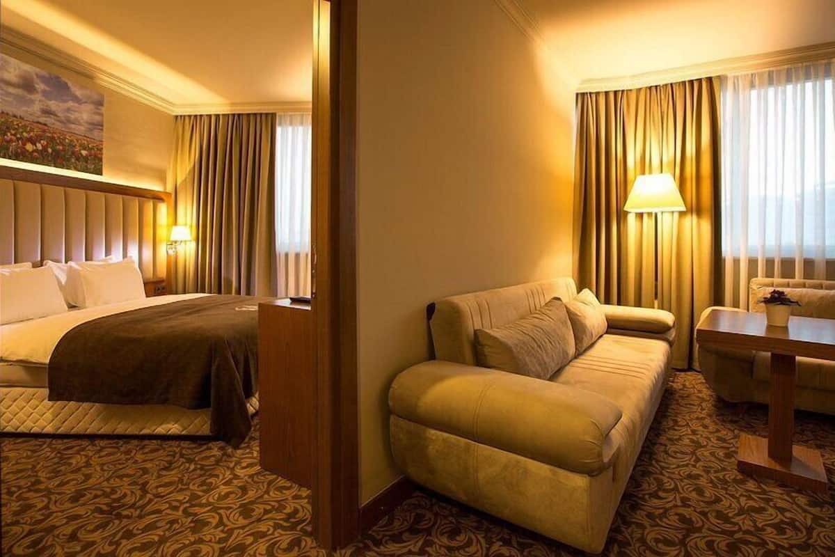Una habitación de hotel con cama, sofá, una mesita y una lámpara.