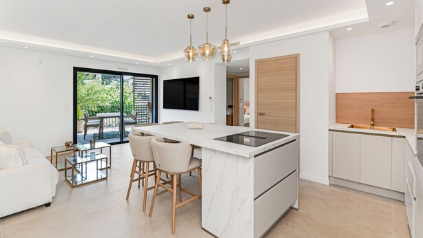 A modern kitchen with a central island, bar stools, and a dining area with a glass table. - Luxury appartement avec parking (Saint-Tropez)