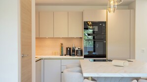 A modern kitchen with a marble countertop, built-in appliances, and a dining area with a white table and grey chairs. - Luxury appartement avec parking (Saint-Tropez)