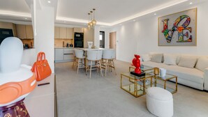 A modern living room with a white sofa, a glass coffee table, and a dining area with a white table and chairs. - Luxury appartement avec parking (Saint-Tropez)