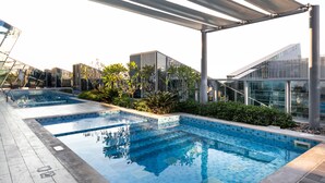 A rooftop pool with clear blue water, surrounded by greenery and modern buildings in the background. - LUX Studio near Burj w Canal Views (Dubai)