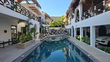 Un área de piscina con una piscina azul cristalina, paredes blancas y techos de paja.