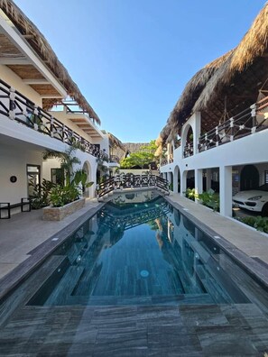 A pool area with a clear blue pool, white walls, and thatched roofs.