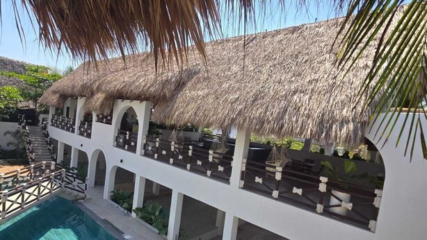 A poolside area with a thatched roof structure, a clear blue pool, and a white building with multiple levels and balconies. - Selanna 3 Luna Creciente (El Paredon)