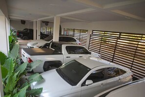 A covered parking area with multiple cars parked in rows, a plant on the left, and a window with blinds on the right.