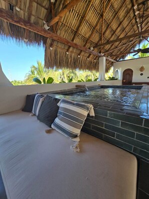 A hot tub area with a thatched roof, a view of palm trees, and a brick wall.
