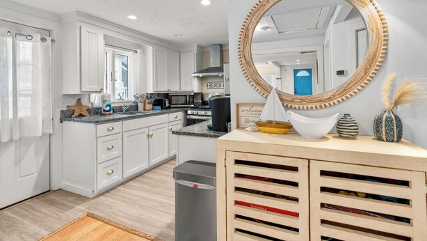 Una cocina moderna con armarios blancos, encimera de granito, un espejo grande y un mueble de madera con cajones.