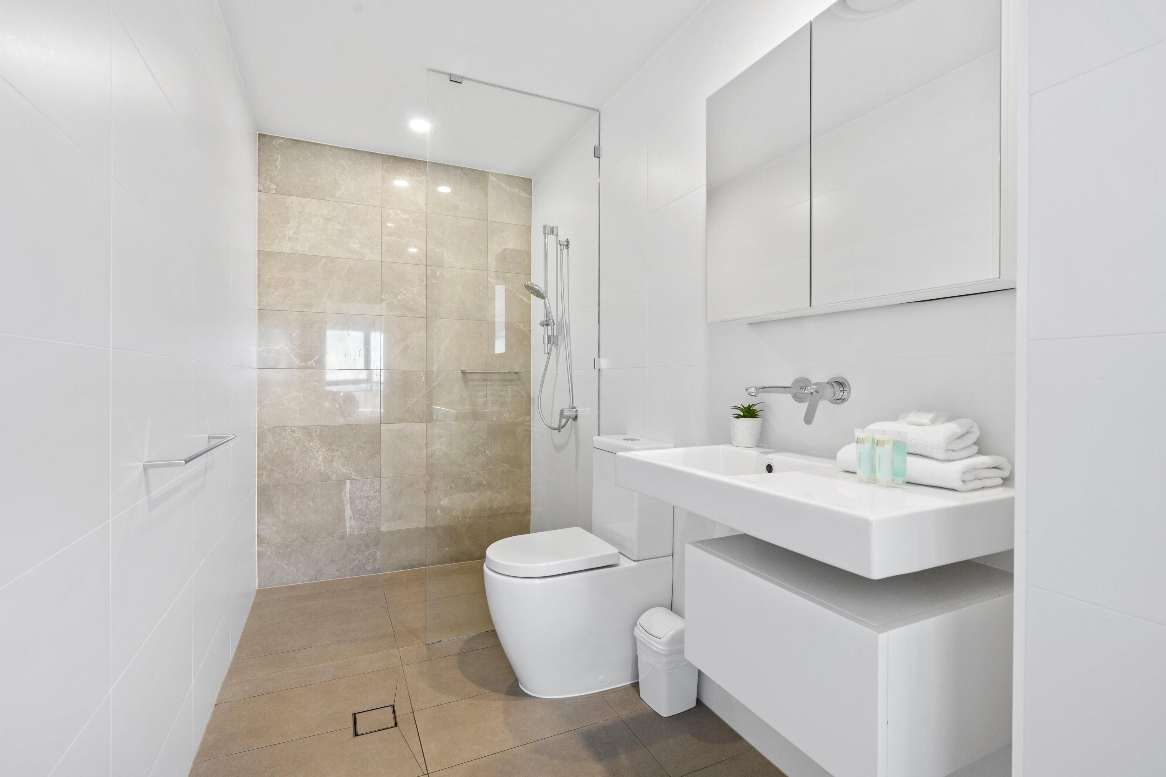 A modern bathroom with a glass shower enclosure, a white toilet, and a vanity with a sink and mirror.