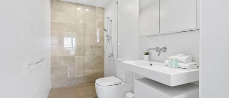 A modern bathroom with a glass shower enclosure, a white toilet, and a vanity with a sink and mirror.