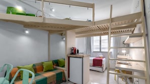 A compact room with a bunk bed, a small kitchenette, a dining area, and a window with curtains.