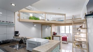 A modern kitchen with a built-in microwave, a sink, and a wooden loft bed with a green blanket.
