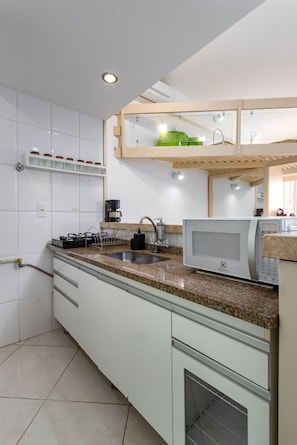 A modern kitchen with white cabinets, a granite countertop, a built-in microwave, and a coffee maker.